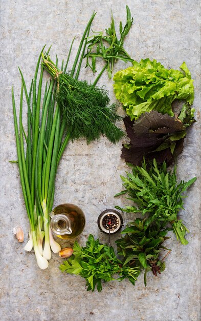 Varietà erbe aromatiche fresche (lattuga, rucola, aneto, menta, lattuga rossa e cipolla) su sfondo grigio in stile rustico. Vista dall&#39;alto