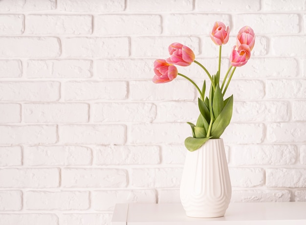 Vaso bianco con bouquet di tulipani rosa sul fondo del muro di mattoni con lo spazio della copia