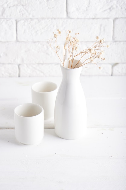 Vaso bianco e tazze su un tavolo bianco Copia spazio verticale
