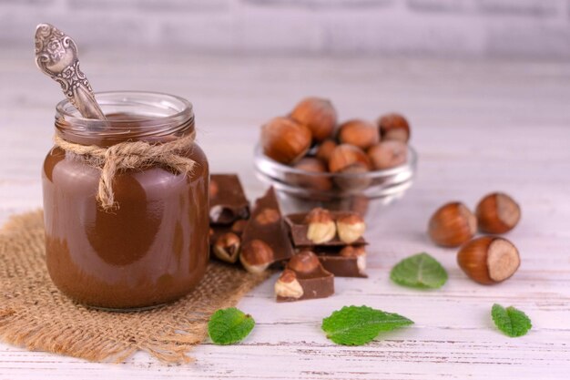 Vaso con cioccolato spalmabile con nocciole su fondo di legno bianco. Primo piano