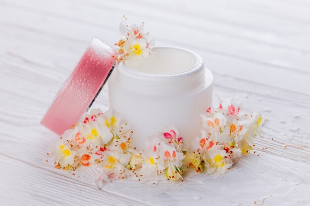 Vaso con crema circondato da fiori. Cosmetici biologici