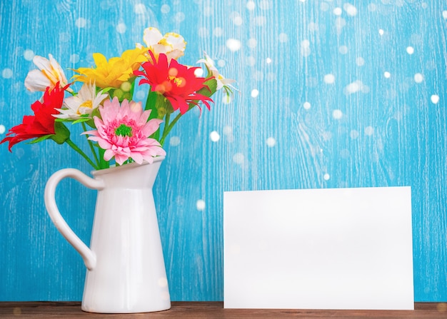 Vaso con fiori e foglio di carta vuoto su uno sfondo di legno