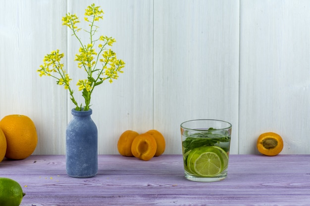 Vaso con fiori gialli di campo, albicocche sul tavolo e un bicchiere di Mojito