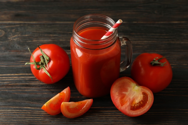 Vaso con succo di pomodoro e paglia e pomodori su fondo in legno