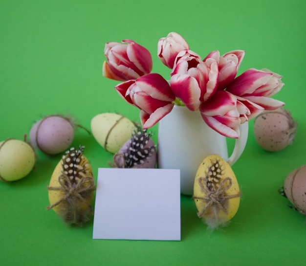 Vaso con tulipani accanto alle uova di Pasqua decorate su uno sfondo verde con spazio per la copia della cartolina