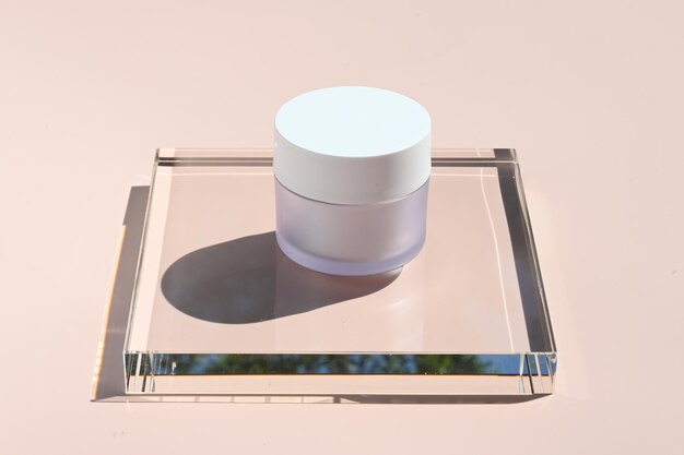 Vaso cosmetico bianco su supporto in vetro su sfondo rosa ai raggi del sole Vaso in vetro bianco per lozione crema o maschera