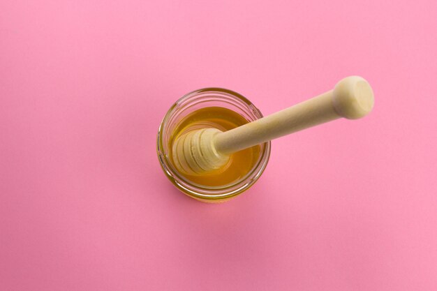 Vaso del miele di vista superiore con il cucchiaio di legno, spazio rosa vibrante della copia del fondo