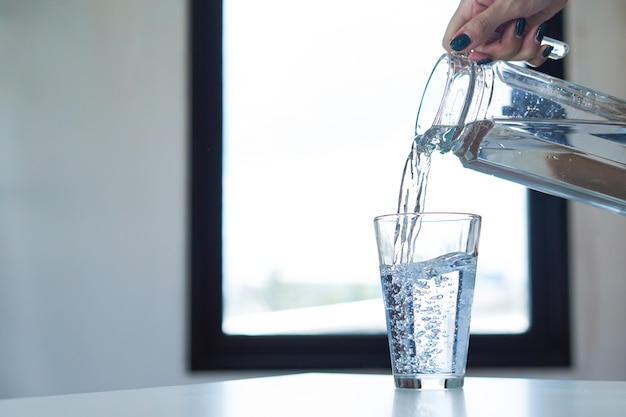 Vaso della holding della mano della donna di acqua e acqua di versamento in un vetro