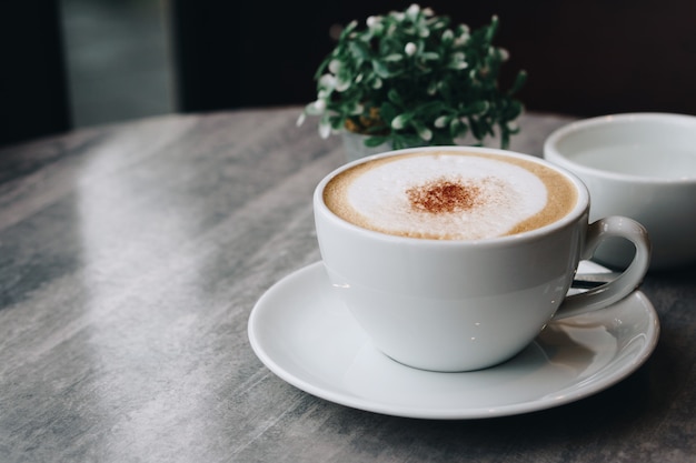 Vaso di fiori e caffè caldo con foglie verdi su un tavolo di marmo