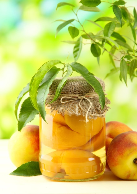 Vaso di pesche in scatola e pesche fresche sul tavolo di legno all'esterno