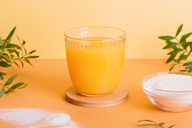 Vaso di succo d'arancia e polvere di collagene su tavolo con pianta e ombra vista dall'alto