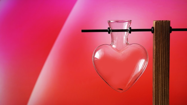 Vaso di vetro a forma di cuore vuoto sul supporto di legno su colore rosso. Vaso di San Valentino