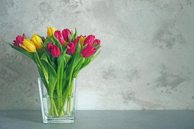 Vaso di vetro con bouquet di bellissimi tulipani su sfondo colorato