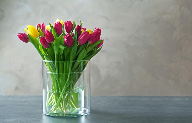 Vaso di vetro con bouquet di bellissimi tulipani su sfondo colorato