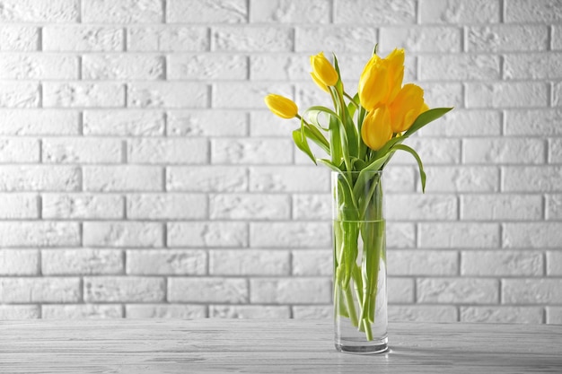 Vaso di vetro con bouquet di bellissimi tulipani su sfondo muro di mattoni