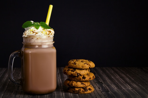 Vaso di vetro con cacao o cioccolata calda, paglia, impilare i biscotti con una briciola di cioccolato, panna montata e ramo di menta