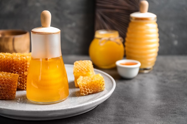 Vaso di vetro con miele delizioso e favi freschi sul tavolo
