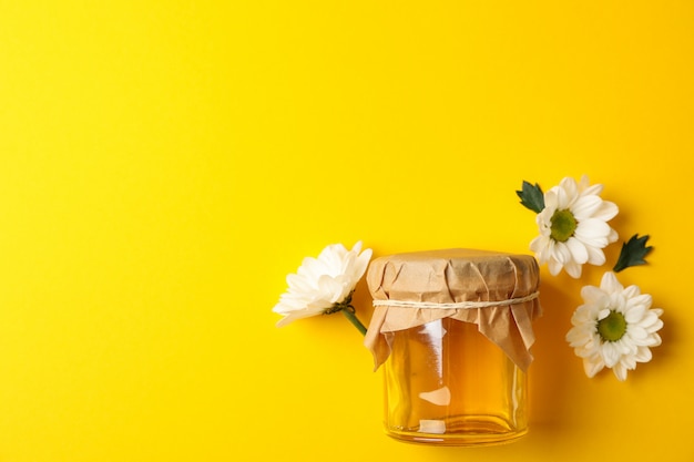 Vaso di vetro con miele e camomilla su sfondo giallo