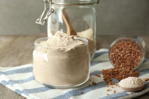 Vaso di vetro e cucchiaio con farina di grano saraceno sul tavolo