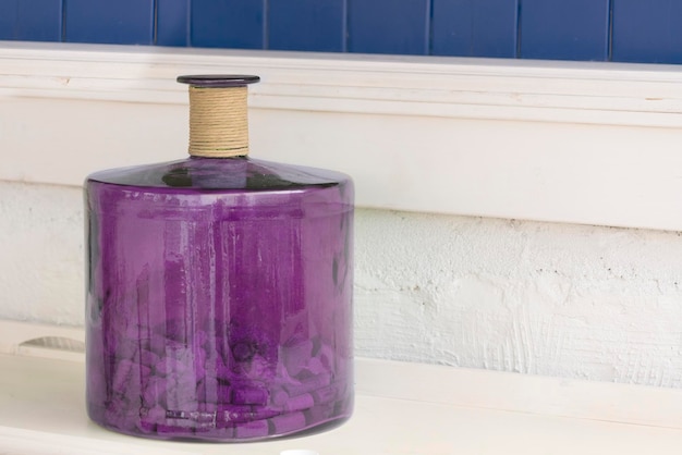 Vaso di vetro viola in piedi vicino a un muro bianco e blu