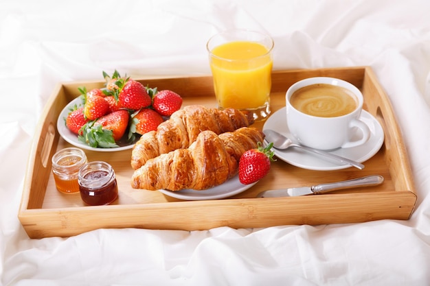 Vassoio colazione a letto, caffè, croissant, succo di frutta e fragole fresche