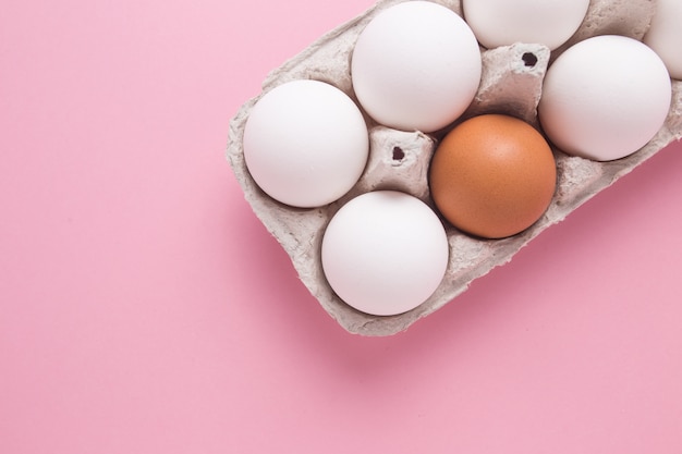 Vassoio con uova di gallina su uno sfondo rosa. Un uovo marrone tra bianco. Il concetto di individualità.