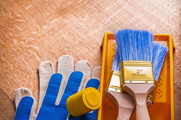 Vassoio delle spazzole del rullo di vernice e guanti protettivi sul concetto di manutenzione della tavola di legno