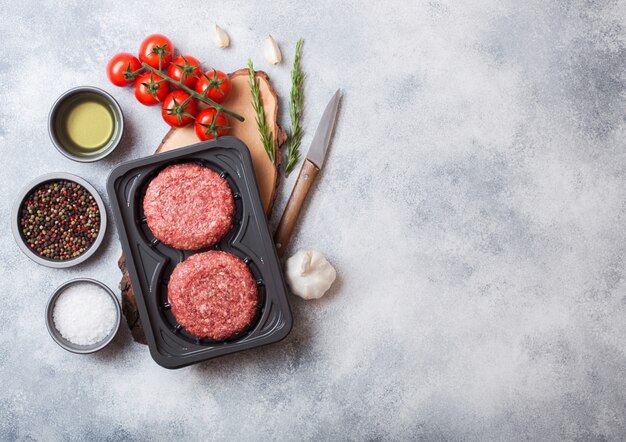 Vassoio di plastica con hamburger di manzo alla griglia tritato crudo fatto in casa con spezie ed erbe aromatiche. Vista dall'alto