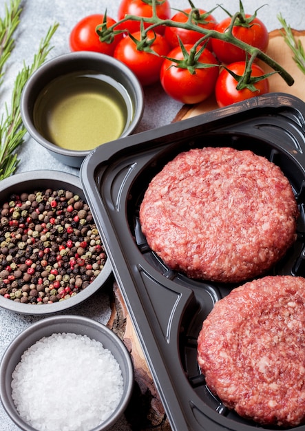 Vassoio di plastica con hamburger di manzo alla griglia tritato crudo fatto in casa con spezie ed erbe aromatiche. Vista dall'alto