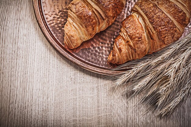 Vassoio di rame per croissant con orecchie di segale di grano maturo su tavola di legno