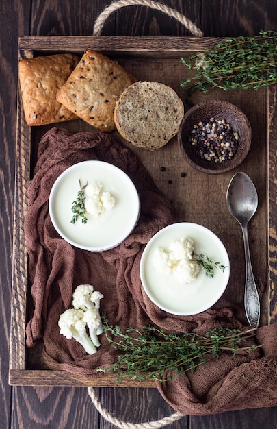 Vassoio in legno con due scodelle in ceramica con contorno di crema di cavolfiore con cavolfiore fresco, timo e pane. Comfort food autunnale o invernale.