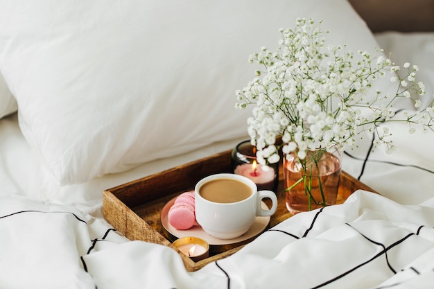 Vassoio in legno di caffè e candele con fiori sul letto. Colazione a letto. concetto di Hygge.