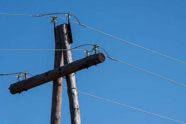 Vecchi cavi del pilone di elettricità sui pali di legno su cielo blu