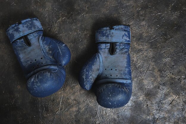 Vecchi guantoni da boxe blu su uno sfondo di cemento.