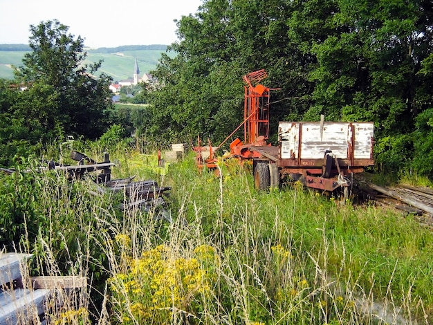 Vecchi macchinari agricoli arrugginiscono vicino ad alberi e campi abbandonati come un'antica macchina agricola