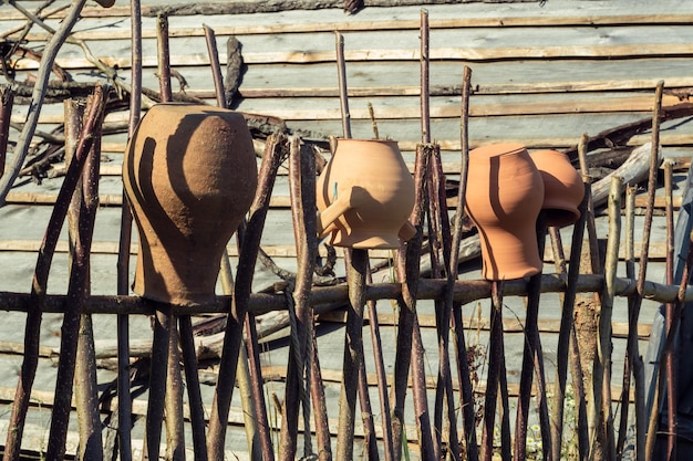 Vecchi vasi di argilla appesi a testa in giù su recinzione di legno Vasi antichi fatti a mano si asciugano all'aperto su pilastri nella soleggiata giornata estiva