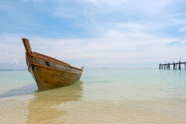 Vecchia barca di legno e mare blu sotto il cielo nuvoloso sulla spiaggia bianca nel giorno soleggiato