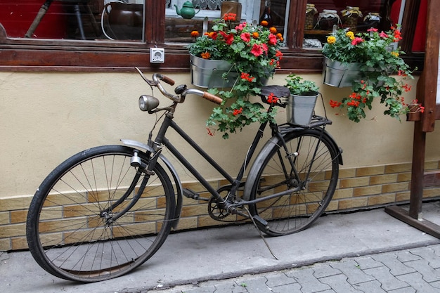 Vecchia bici nera vicino all'accogliente caffè con fiori rossi e arancioni