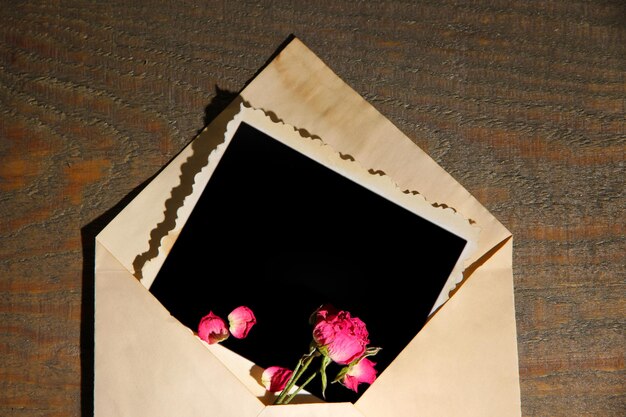 Vecchia busta con carta fotografica in bianco e belle rose secche rosa su fondo di legno