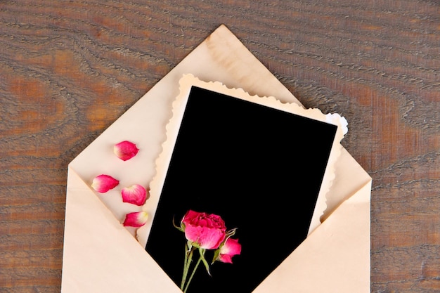 Vecchia busta con carta fotografica in bianco e belle rose secche rosa su fondo di legno