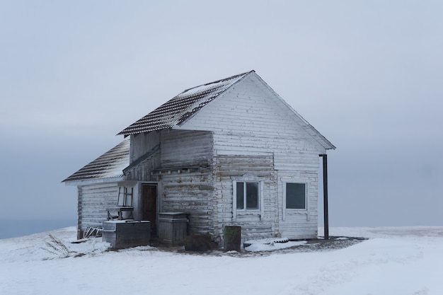 Vecchia casa di legno in cima a una montagna in un paesaggio desertico invernale innevato