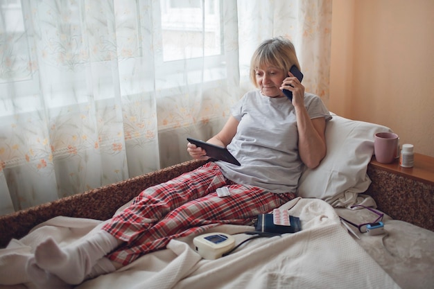 Vecchia donna a letto guardando lo schermo del laptop e consulenza con un medico online a casa, telemedicina