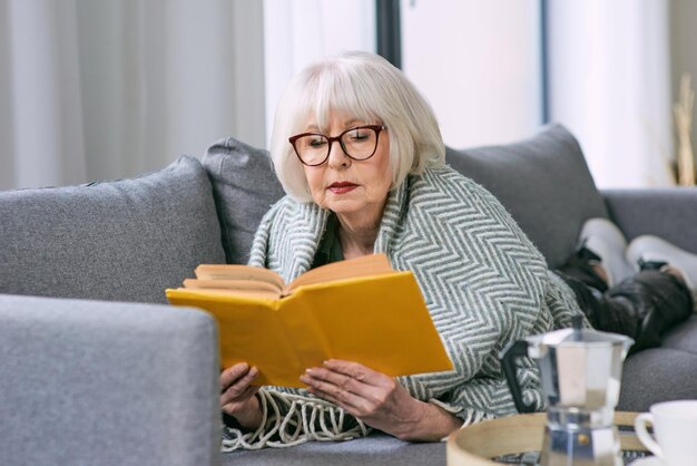 vecchia donna anziana sdraiata sul divano a leggere un libro