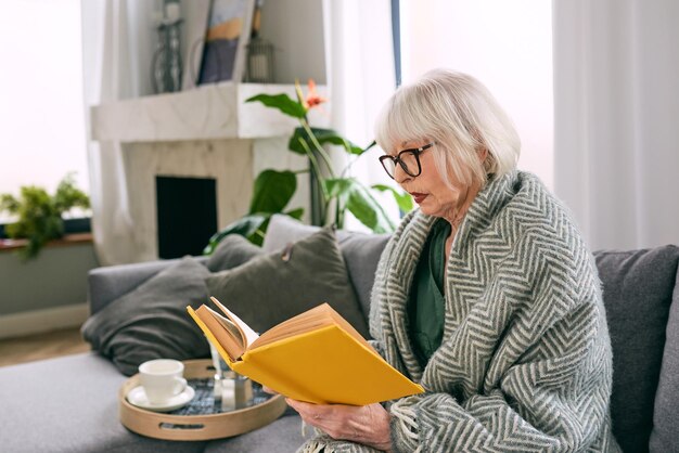 vecchia donna anziana seduta sul divano a leggere un libro a casa