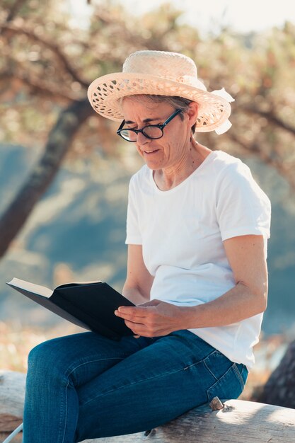 Vecchia donna che legge un libro in spiaggia durante una giornata di sole super. Concetto di libertà con copia spazio, relax e felicità pensionistica senior retirement