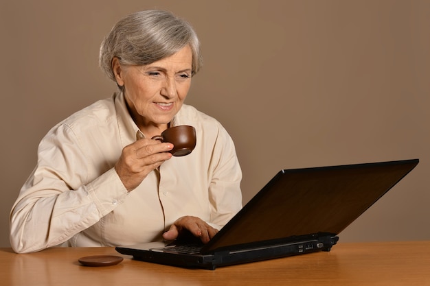 Vecchia donna con un computer portatile e caffè sullo sfondo