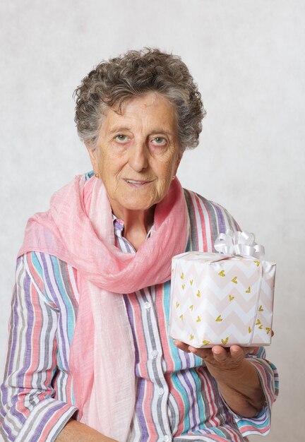 Vecchia donna tra i 70 e gli 80 anni con sciarpa rosa e regalo di qualcuno