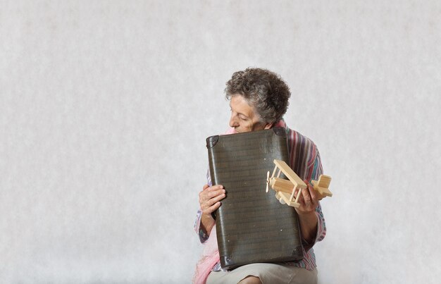 Vecchia donna tra i 70 e gli 80 anni con sciarpa rosa e valigia vintage