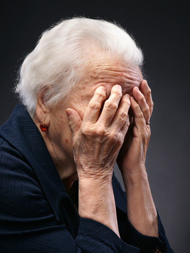 Vecchia donna triste in posa in studio su sfondo grigio