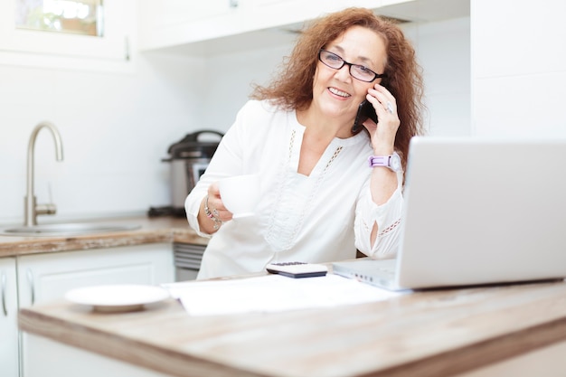 vecchia donna usando il suo smartphone in cucina.